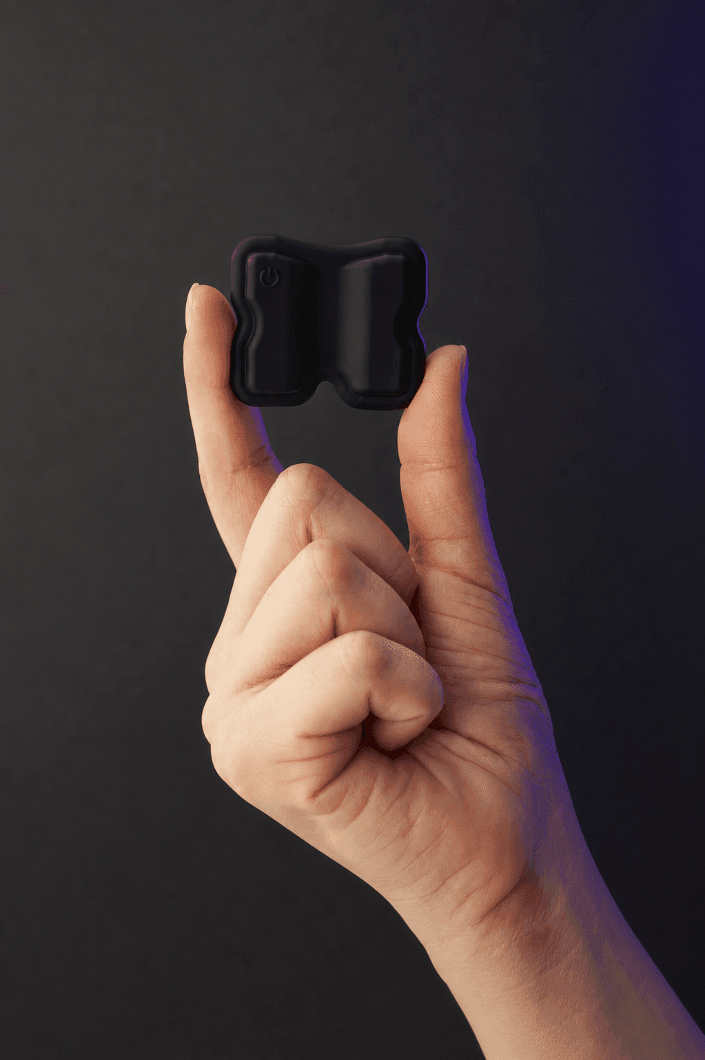 Black KTRL Portable Smart Patch held between two fingers, showing its compact size and power button.
